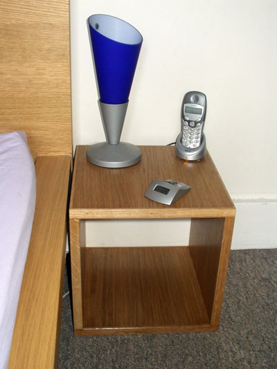 One of a pair of bedside tables next to a matching bed. A contemporary style blue lamp is placed on the table