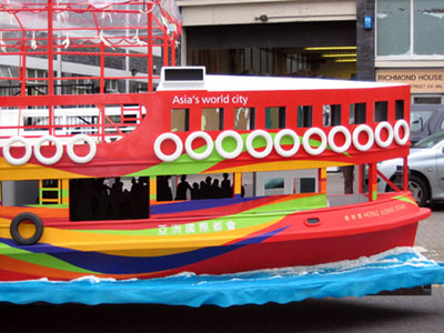 Side view of a red boat with yellow, green and blue wavy stripes on the hull and a large glassed-in promenade deck