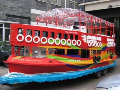 Three-quarter view of a parade float in the form of a large red boat on carved waves, mounted on a trailor