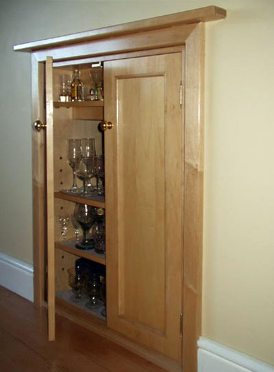 Three-quarter view of a built-in drinks cabinet with three shelves, one door open and one closed