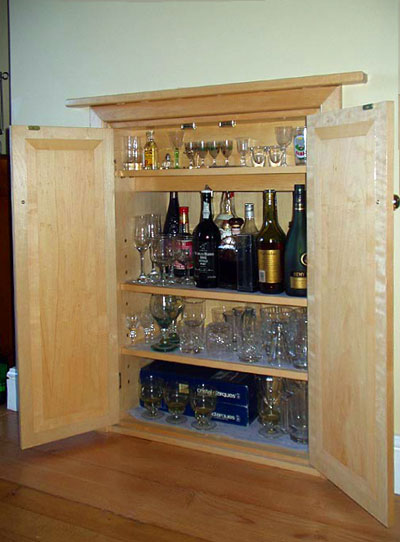 Three-quarter view of a built-in drinks cabinet with three shelves, the doors open to show the interior with bottles and glasses
